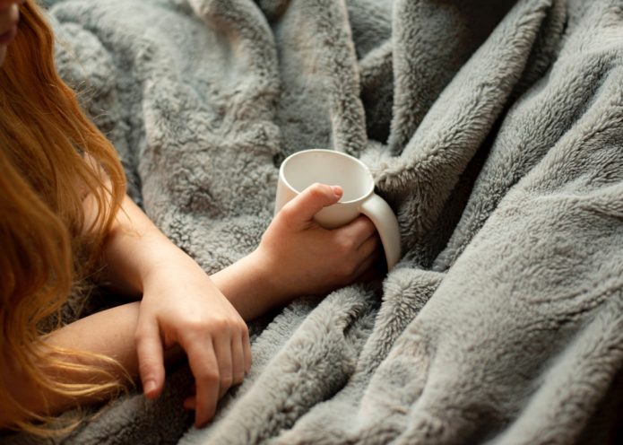 A person holds a coffee cup on a cosy blanket.